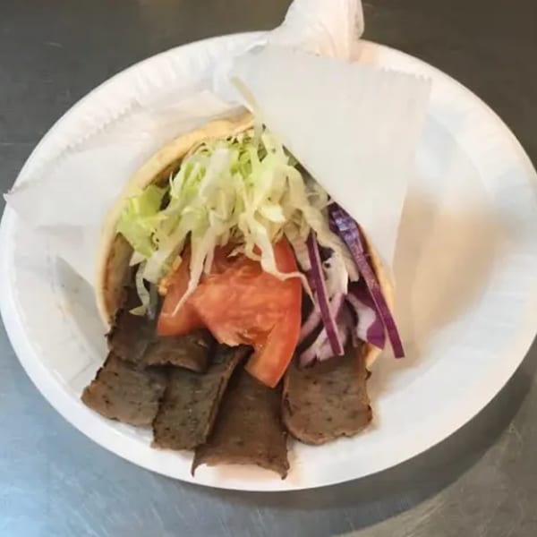 A Voulapitta Greek Restaurant gyro with meat, lettuce, tomatoes, and red onions on a white plate.