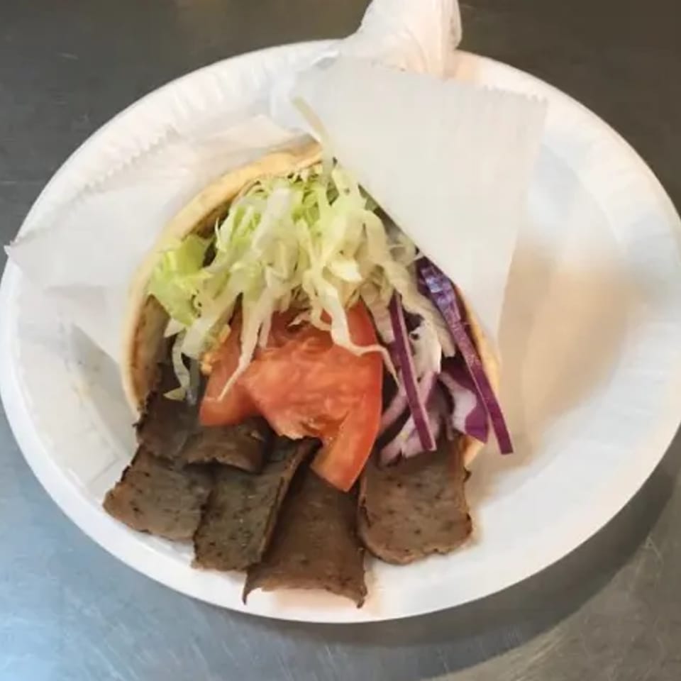 A Voulapitta Greek Restaurant gyro with meat, lettuce, tomatoes, and red onions on a white plate.