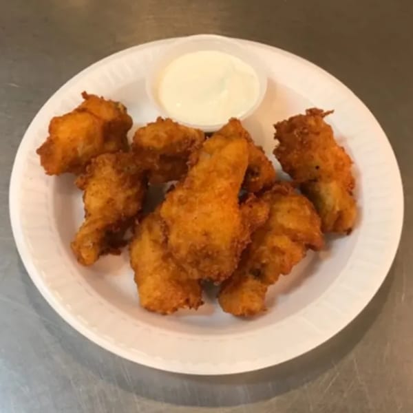 Crispy fried chicken pieces with a side of creamy white dipping sauce on a white plate.