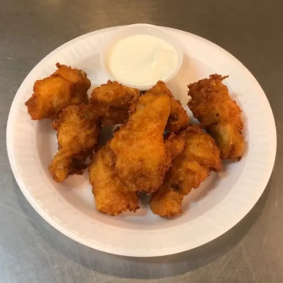 Crispy fried chicken pieces with a side of creamy white dipping sauce on a white plate.