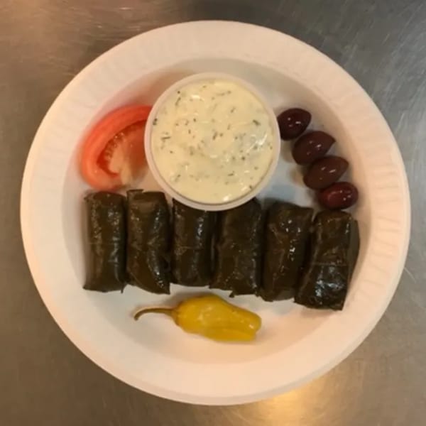 A Greek appetizer plate with dolmades, tzatziki, tomato, olives, and a yellow pepper.