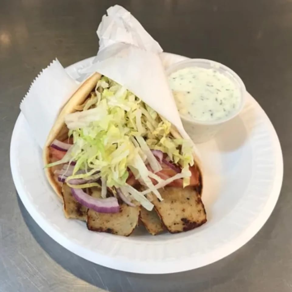 A Voulapitta Greek Restaurant gyro with meat, lettuce, onions, and tomatoes, served with tzatziki sauce.