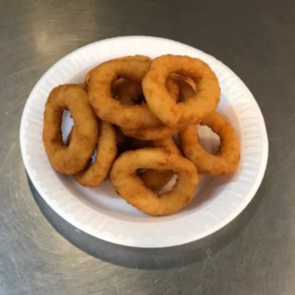 Golden-brown onion rings piled on a white paper plate, ready to be served at Voulapitta Greek Restaurant.